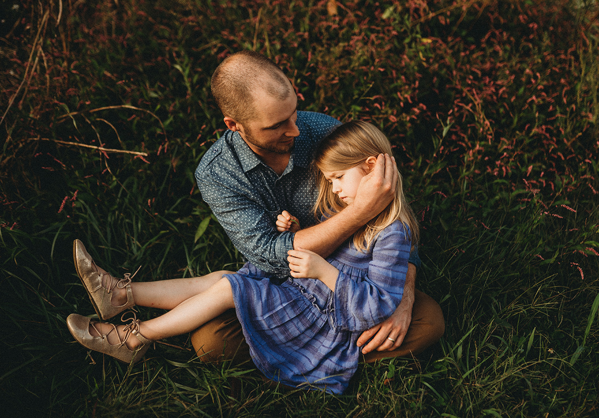 father and daughter sharing a quiet moment as he tucks her hair behind her ear sitting in tall grass