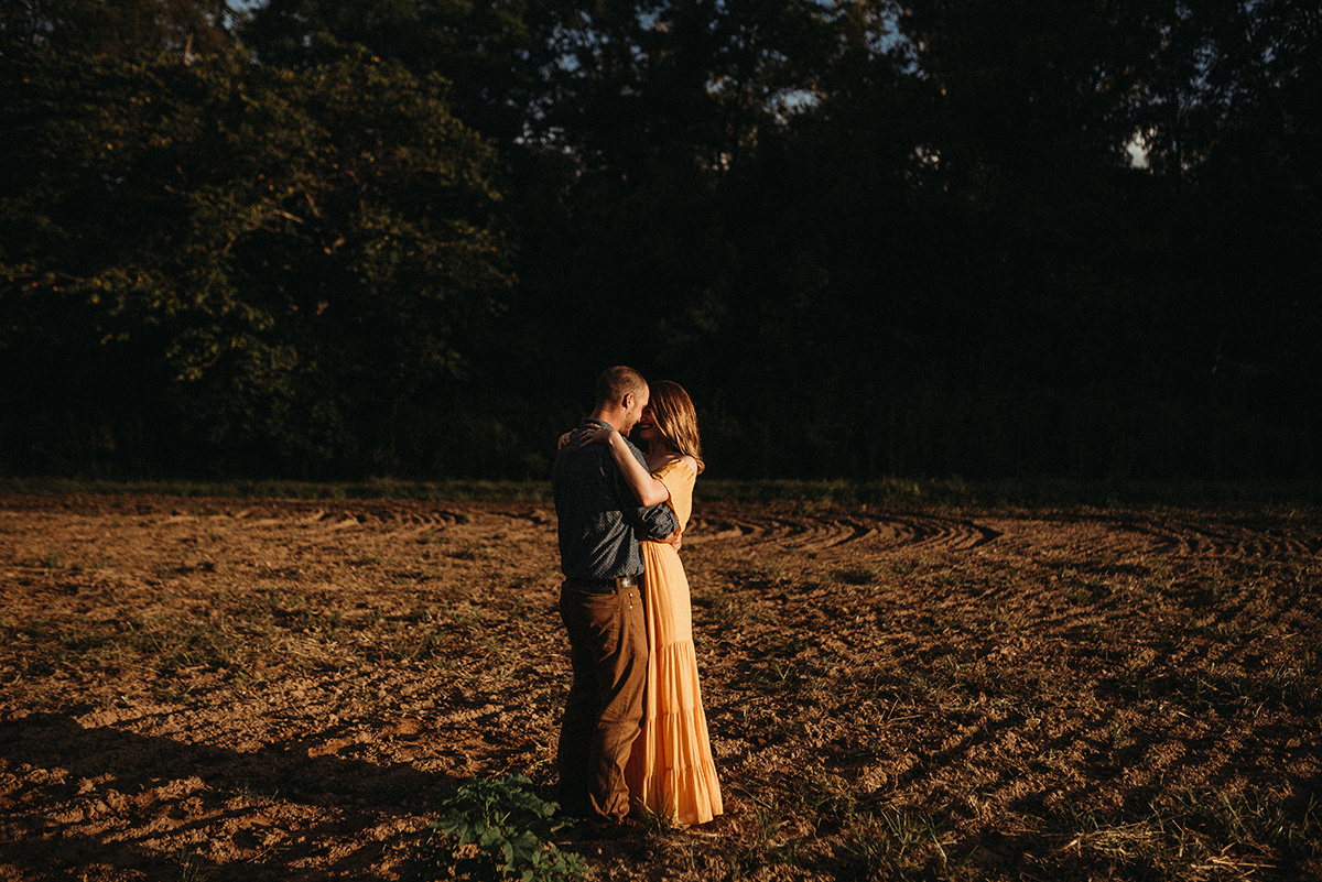 intimate moment between a couple embracing with foreheads together in direct light standing in a dirt field