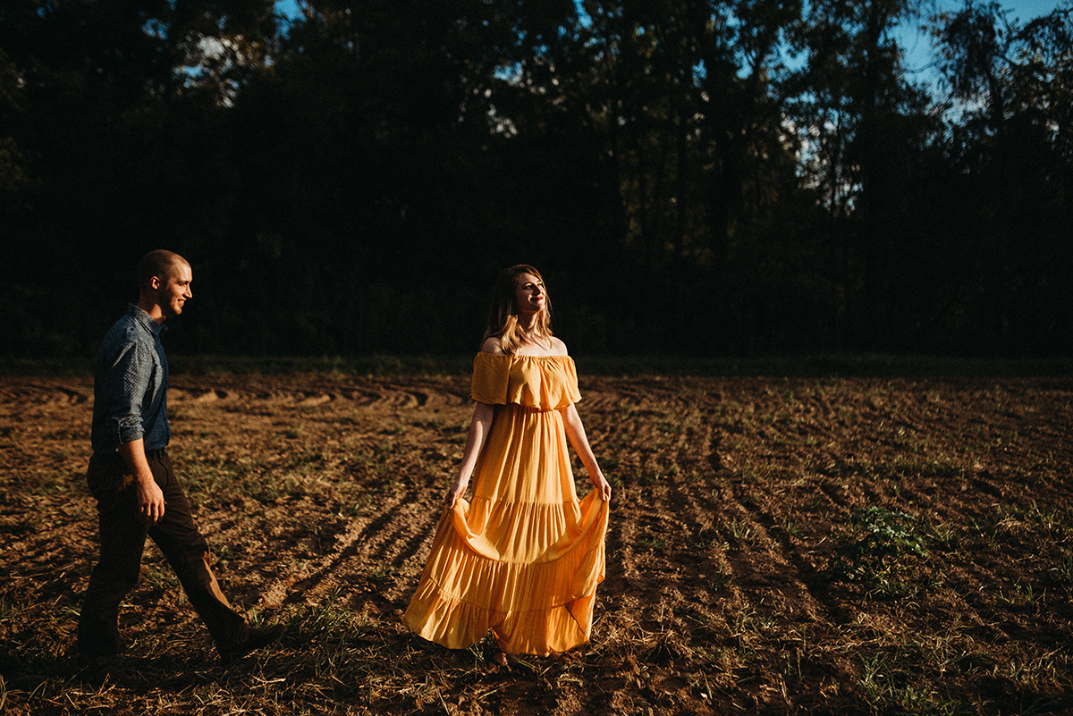 man walking towards his wife in a yellow dress dancing in a dirt field in the direct sunlight
