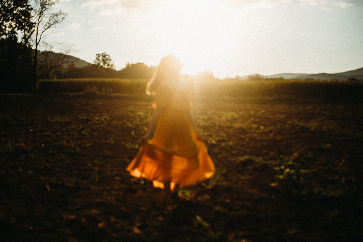 out of focus photo of a mother wearing a yellow dress dancing in a dirt field drenched in beautiful golden backlight