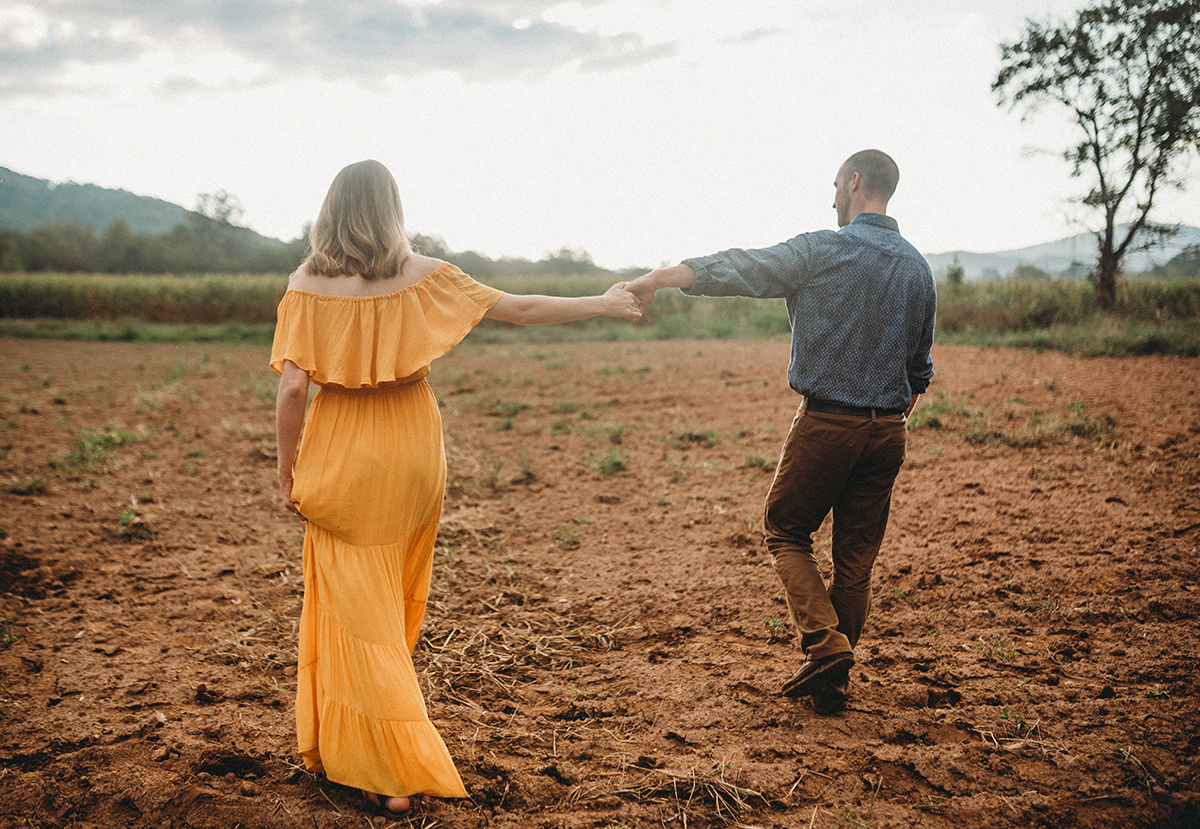 Parents holding hands, while walking through a dirt field
