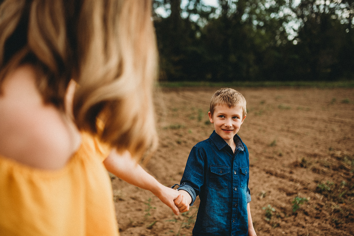 son smiling at his mother and holding her hand while standing in a field of dirt