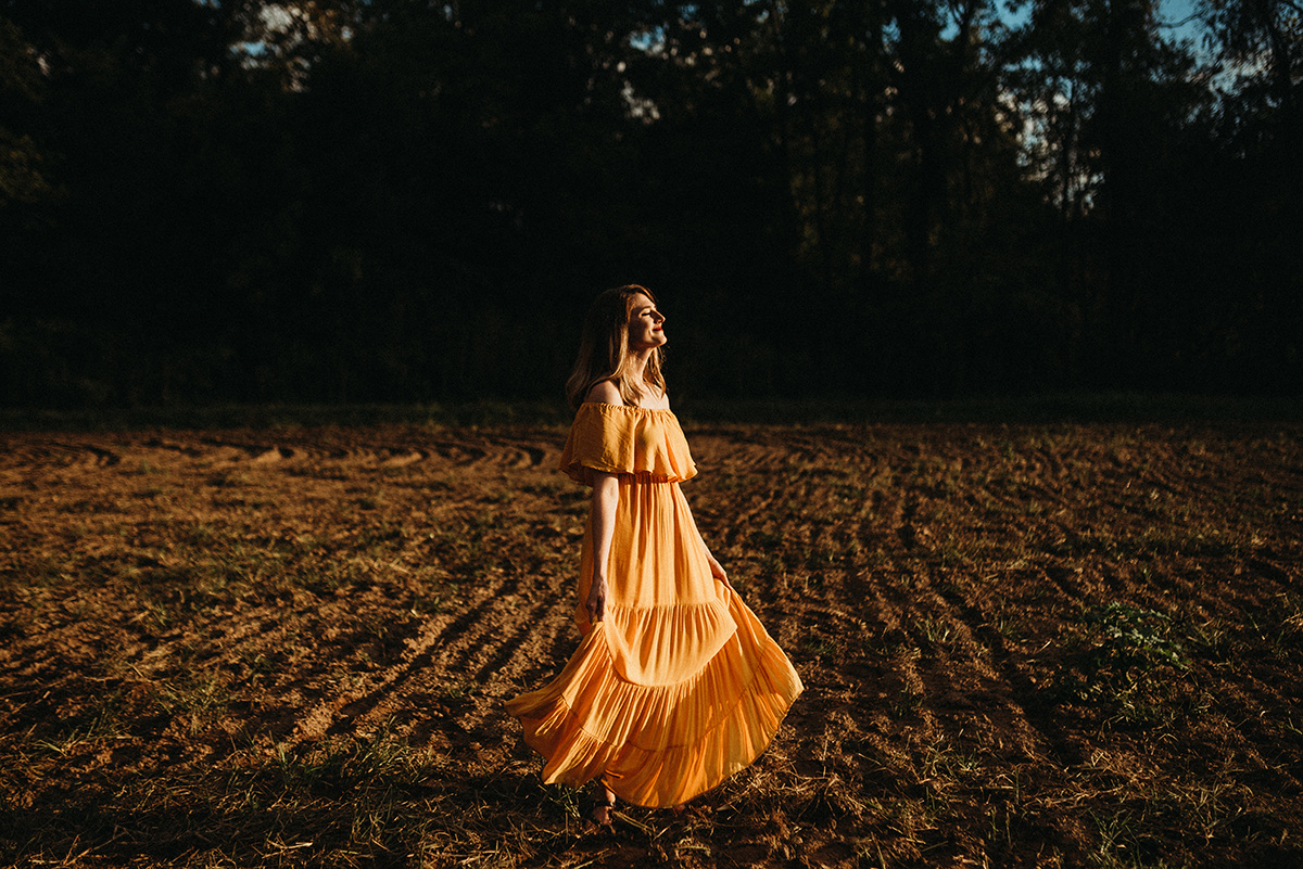 woman in a yellow dress dancing in a dirt field in the direct sunlight